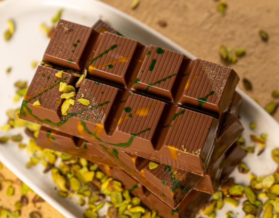 Stacked milk chocolate bars with pistachio pieces, drizzled with green and orange.